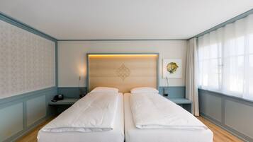 Cama de casal com lençóis brancos em quarto com paredes azul claro e chão de madeira.