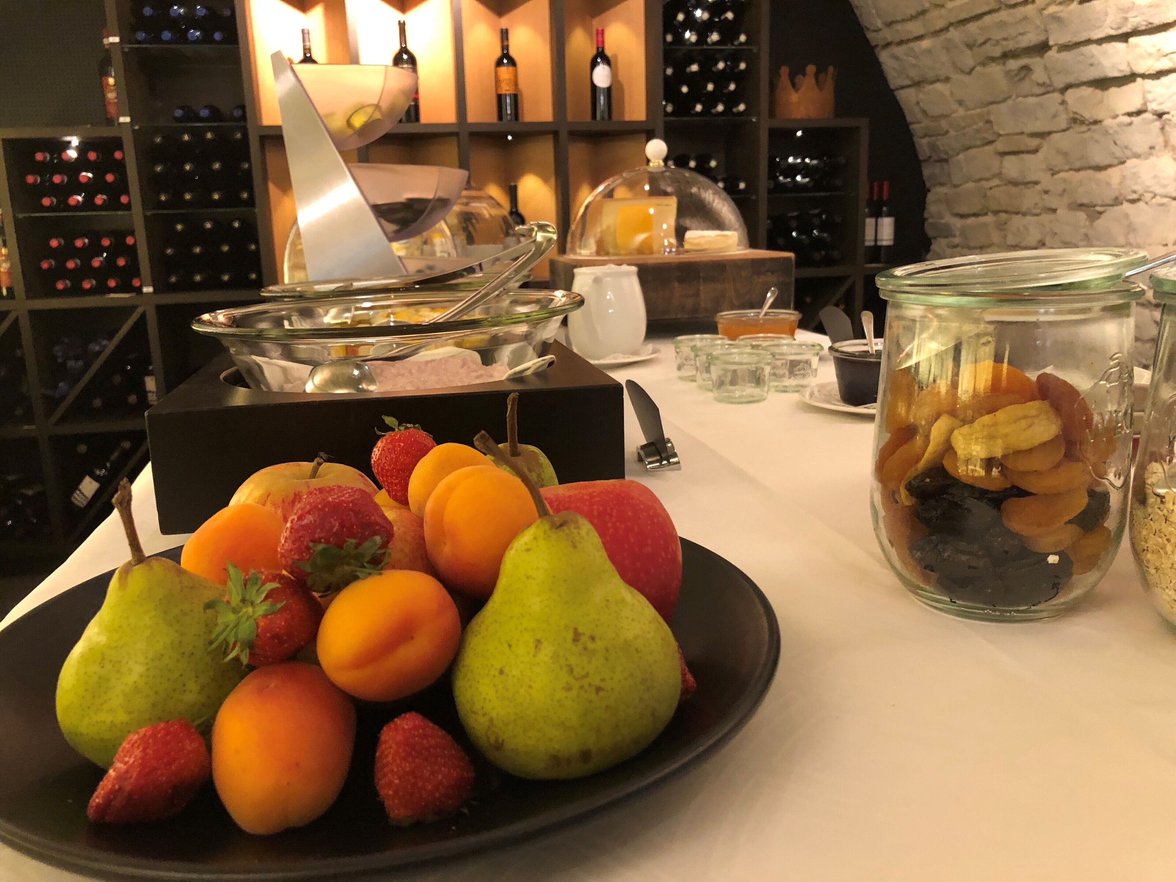 A buffet table with a variety of fruits and a glass jar filled with nuts.