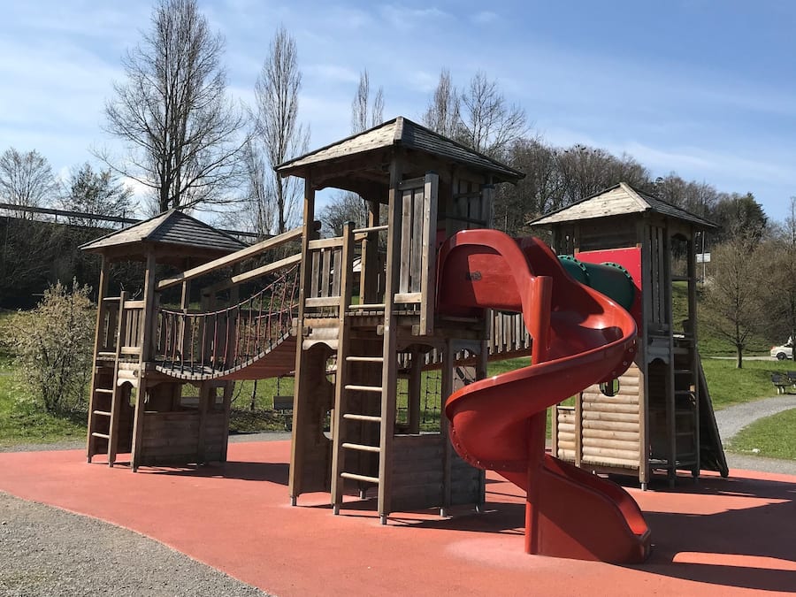 A playground with a red spiral slide and wooden climbing structures.