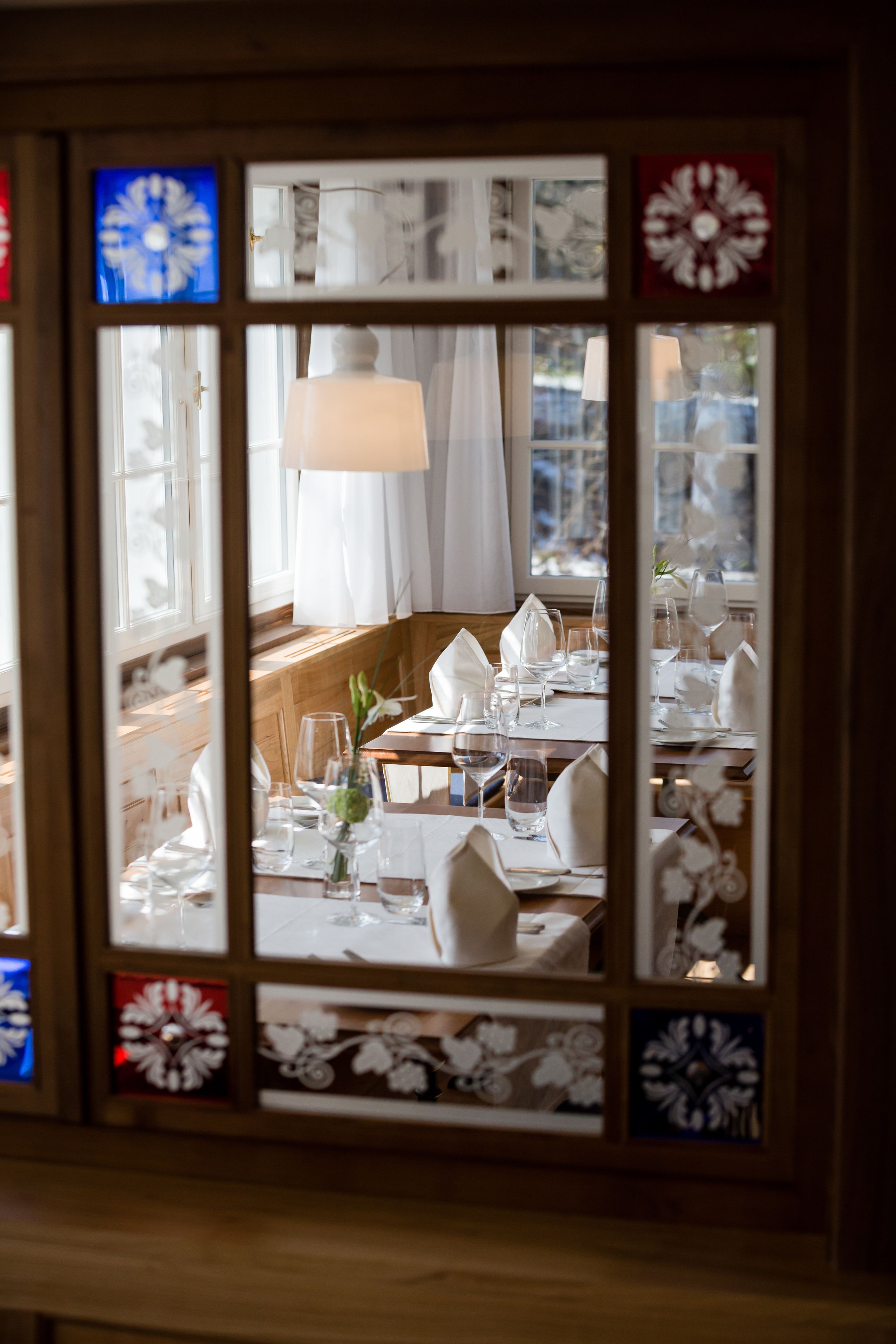 A dining area with tables set for service, a large window with decorative glass panes, and a view of the outside.