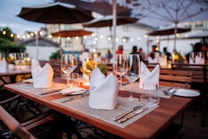 A dining table set with white napkins, wine glasses, and cutlery, with umbrellas and string lights in the background. - Hotel Krone Speicher (Speicher)