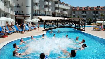 Una piscina con un puente de madera, sillas de descanso y sombrillas.