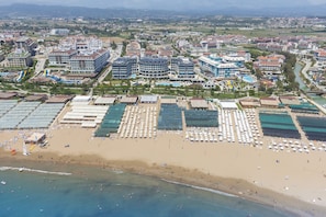 Vue aérienne d’une station balnéaire comprenant plusieurs bâtiments d’hôtel, une plage de sable et un port de plaisance.