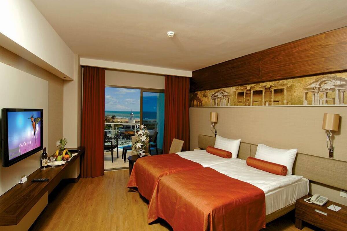 A hotel room with a large bed, a TV, a desk with a fruit tray, and a view of the ocean.