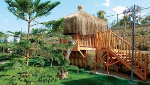 A thatched-roof structure with wooden stairs leading to a platform, surrounded by lush greenery. - Commodore Elite Suites & Spa - All Inclusive - Adult Only (Manavgat)