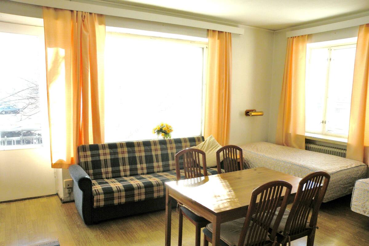 Une pièce comprenant un canapé, une table à manger avec des chaises, un lit et de grandes fenêtres avec des rideaux.