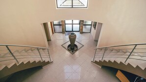 Un interior espacioso con una fuente decorativa central, una escalera con barandillas de metal y grandes ventanales que dejan entrar luz natural.