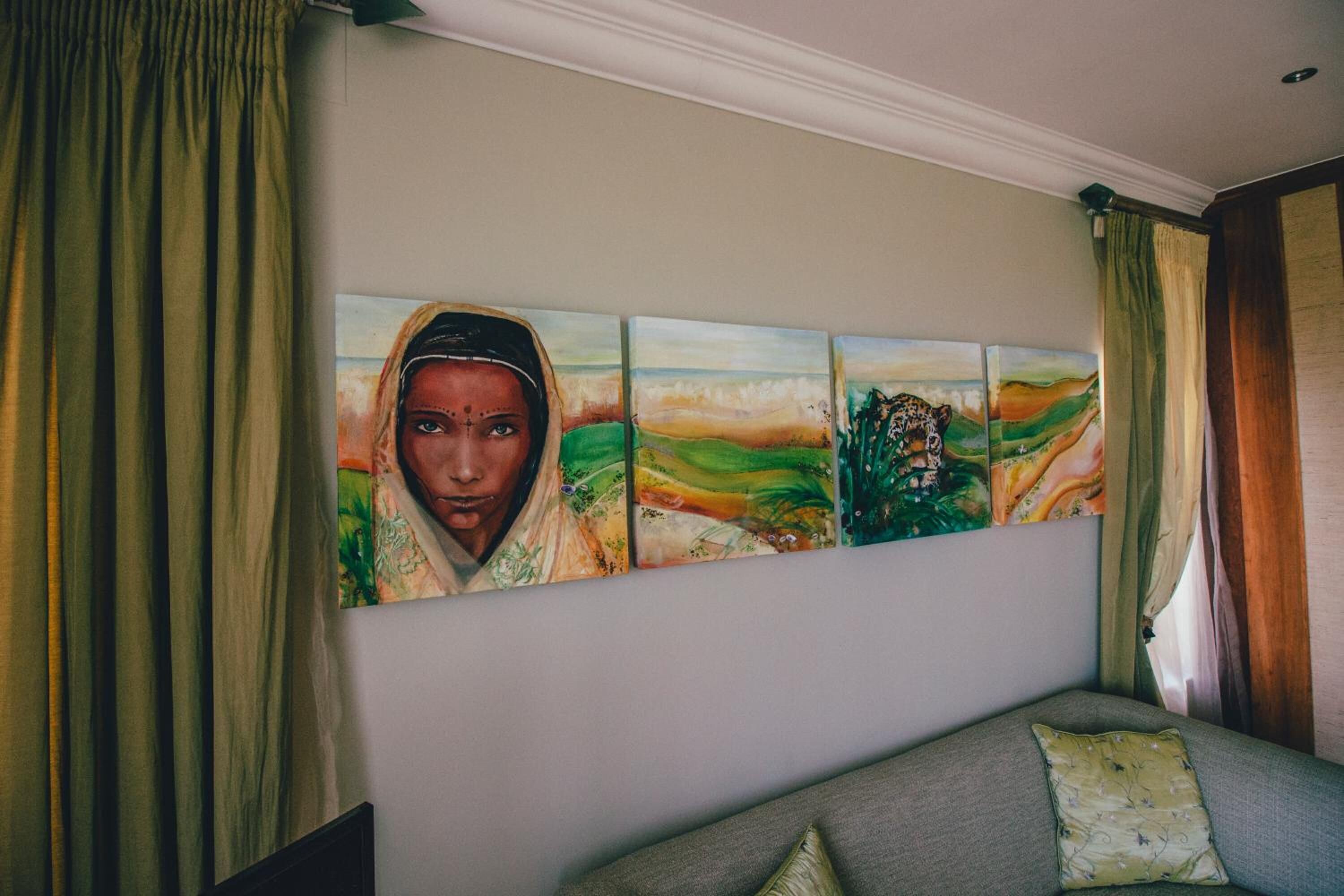 A bedroom with a large painting on the wall, a grey sofa, and green curtains.