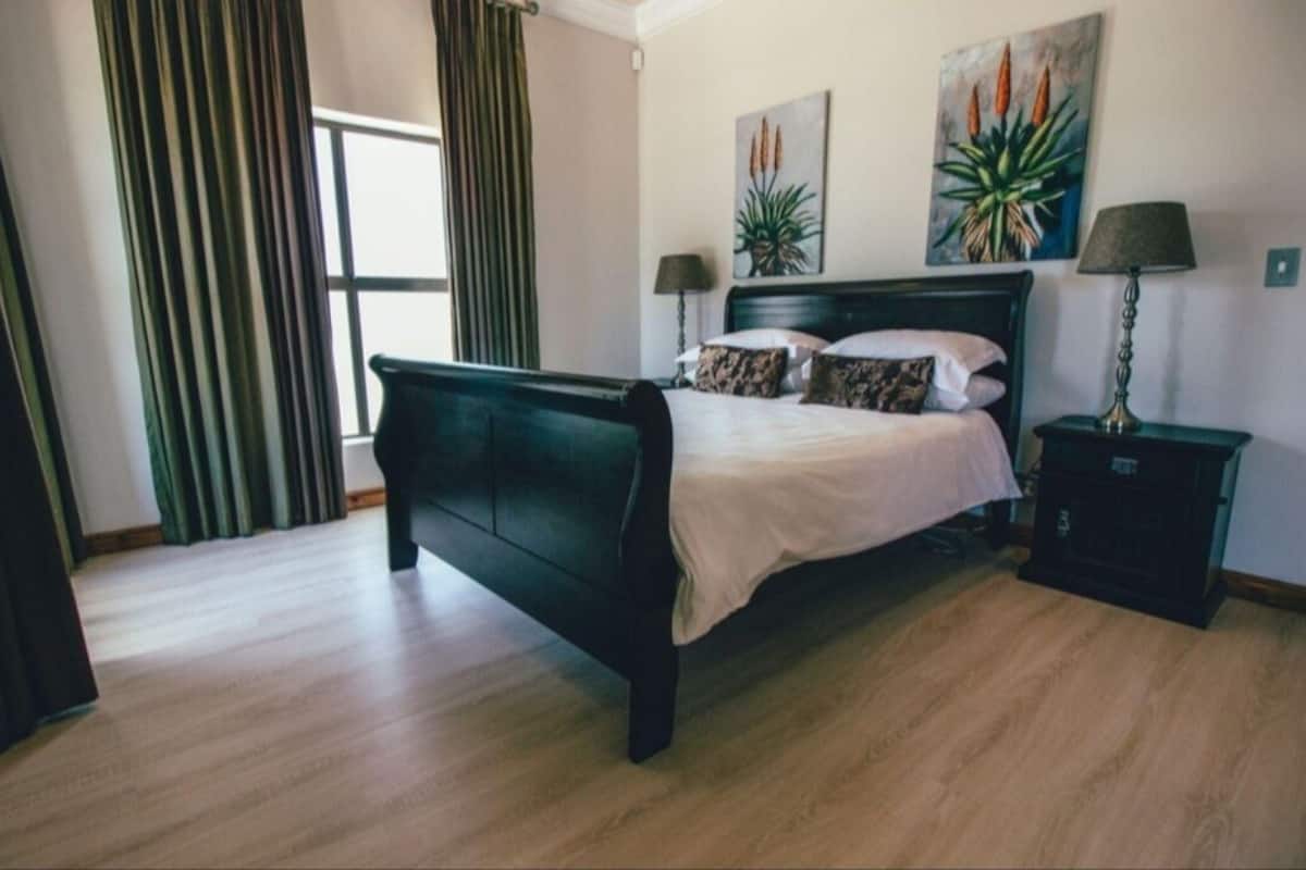 A bedroom with a dark wooden bed, two bedside tables with lamps, a window with curtains, and two wall-mounted paintings.
