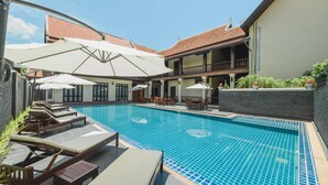 A swimming pool with lounge chairs and umbrellas, surrounded by a building with a tiled roof. - Sada Hotel (Luang Prabang)
