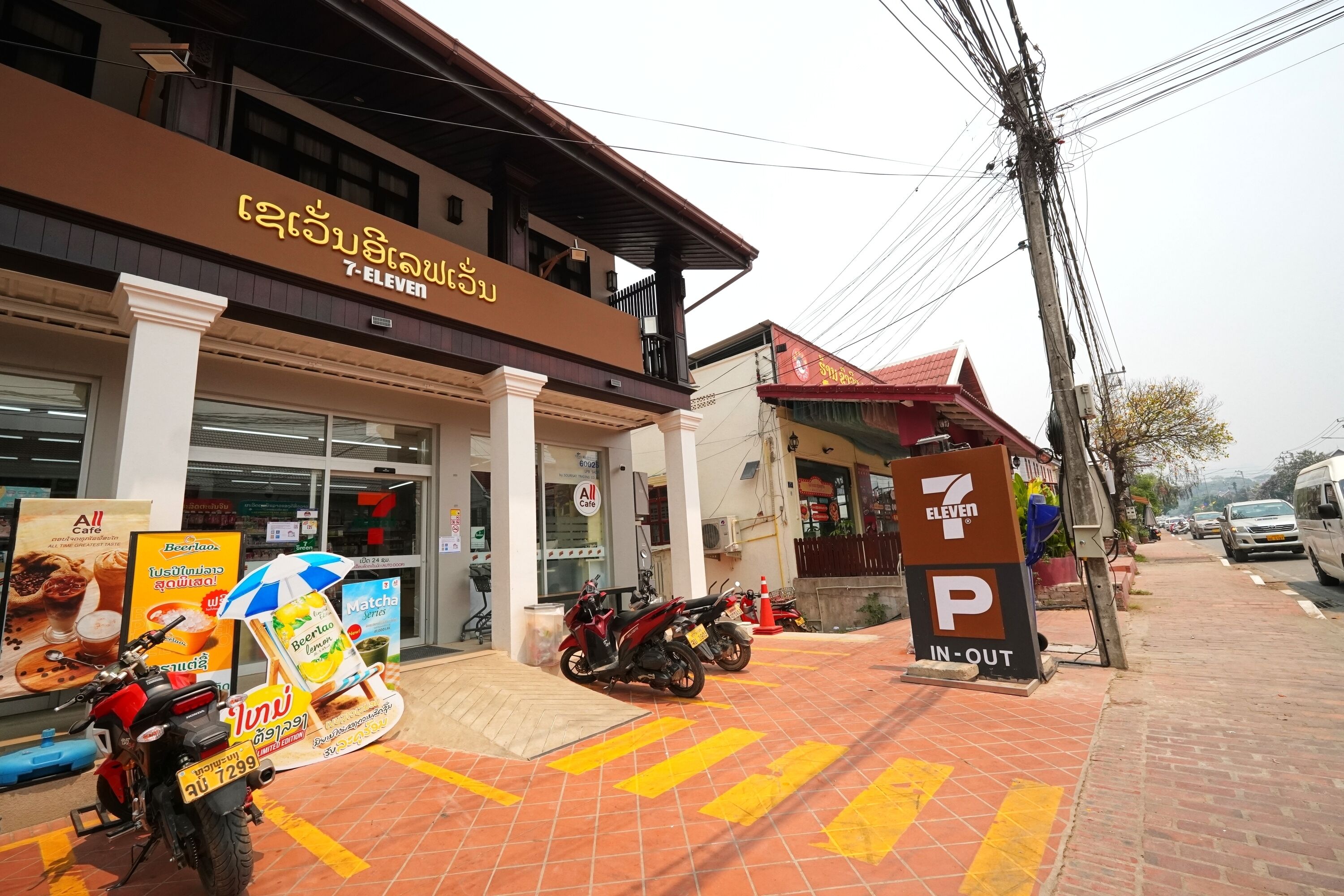 A 7-Eleven convenience store with a parking sign, a motorcycle, and a pedestrian crossing.