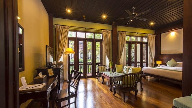 A room with a wooden floor, a bed, a desk with a chair, and a dining table with chairs. - Sada Hotel (Luang Prabang)
