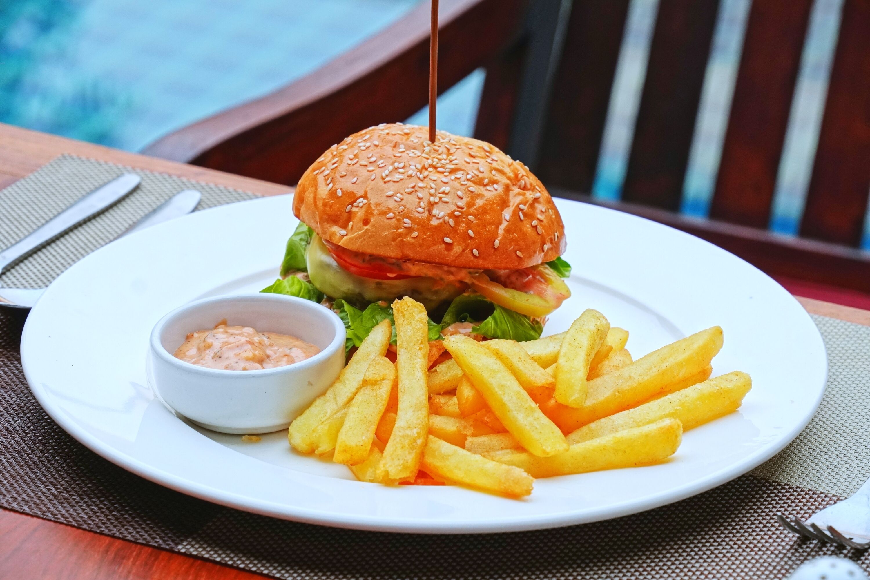 Un plato con una hamburguesa, papas fritas y un recipiente pequeño con salsa.
