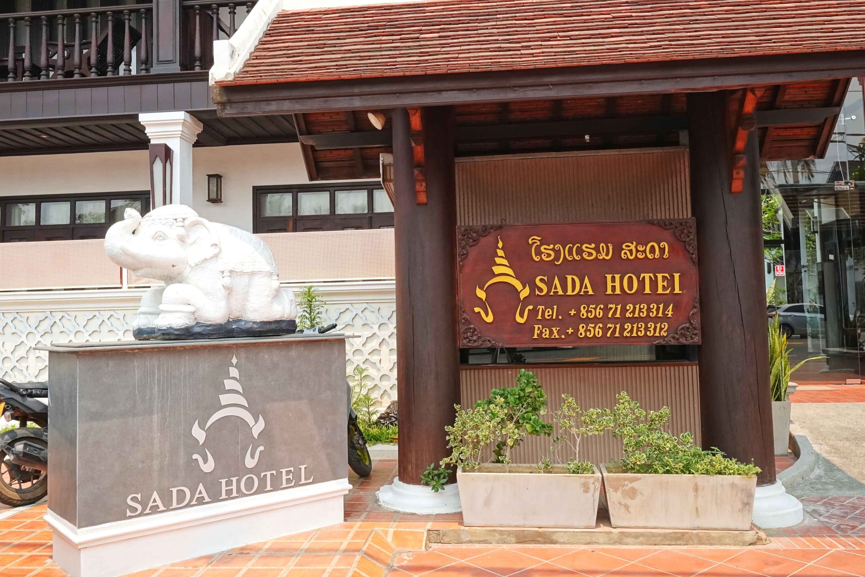 A hotel entrance with a signboard displaying the name 'SADA HOTEL' and contact information.