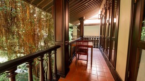A covered balcony with wooden railings, a tiled floor, and a chair. - Sada Hotel (Luang Prabang)
