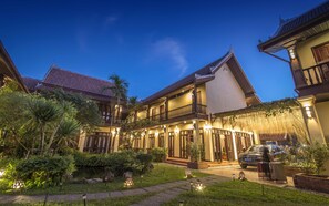 A traditional two-story building with a balcony, surrounded by lush greenery and a paved pathway. - Sada Hotel (Luang Prabang)