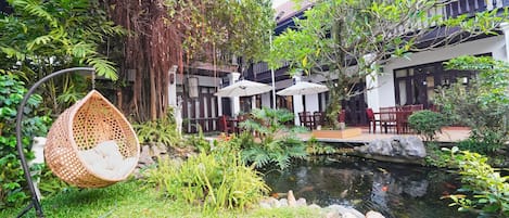 A garden with a hanging chair, a pond with fish, and outdoor seating.