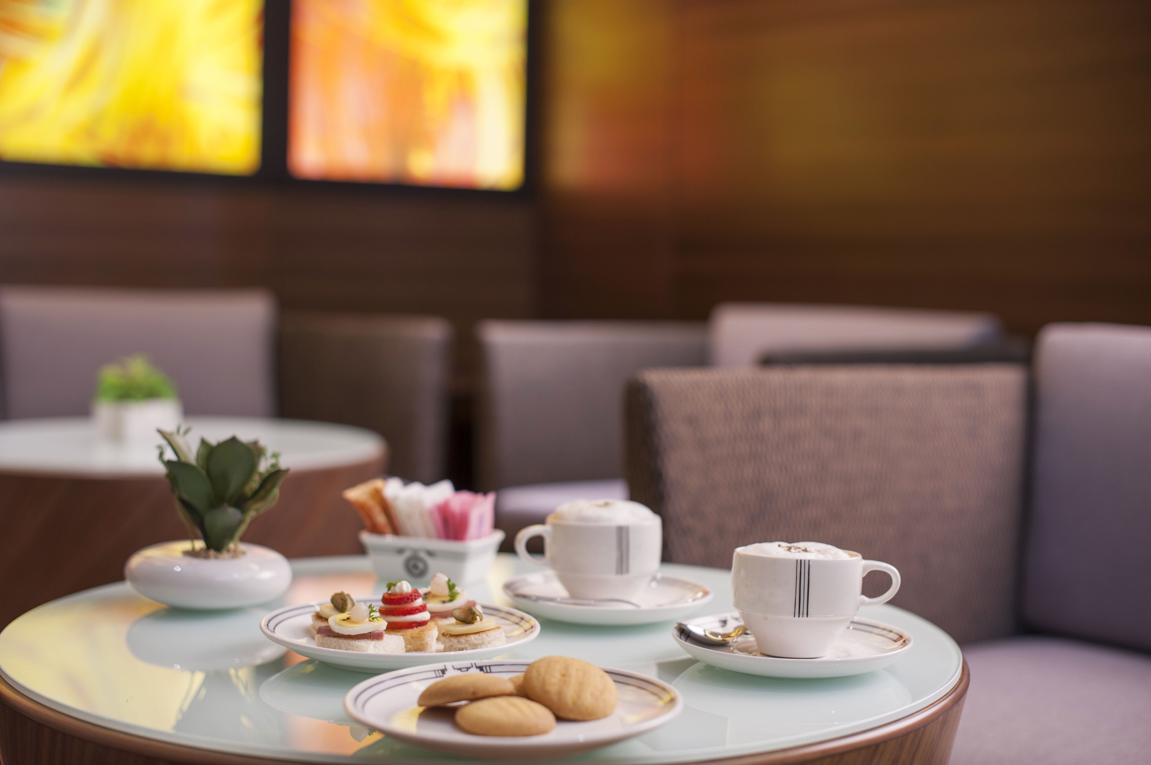 A round table with a variety of pastries and cups, likely a tea or coffee service, in a modern interior with neutral tones and a comfortable seating area.