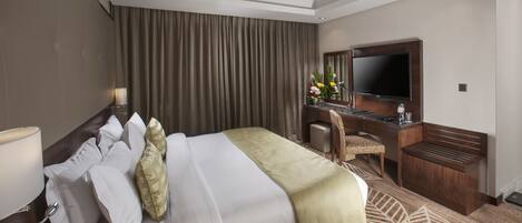 A hotel room with a large bed, a desk, a chair, a TV, and a mirror.