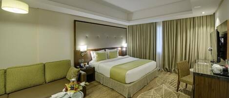 A hotel room with a large bed, a sofa, a desk, and a mirror.