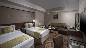 Habitación de hotel con dos camas, un sofá, un escritorio y un televisor de pantalla plana, además de una cafetera.