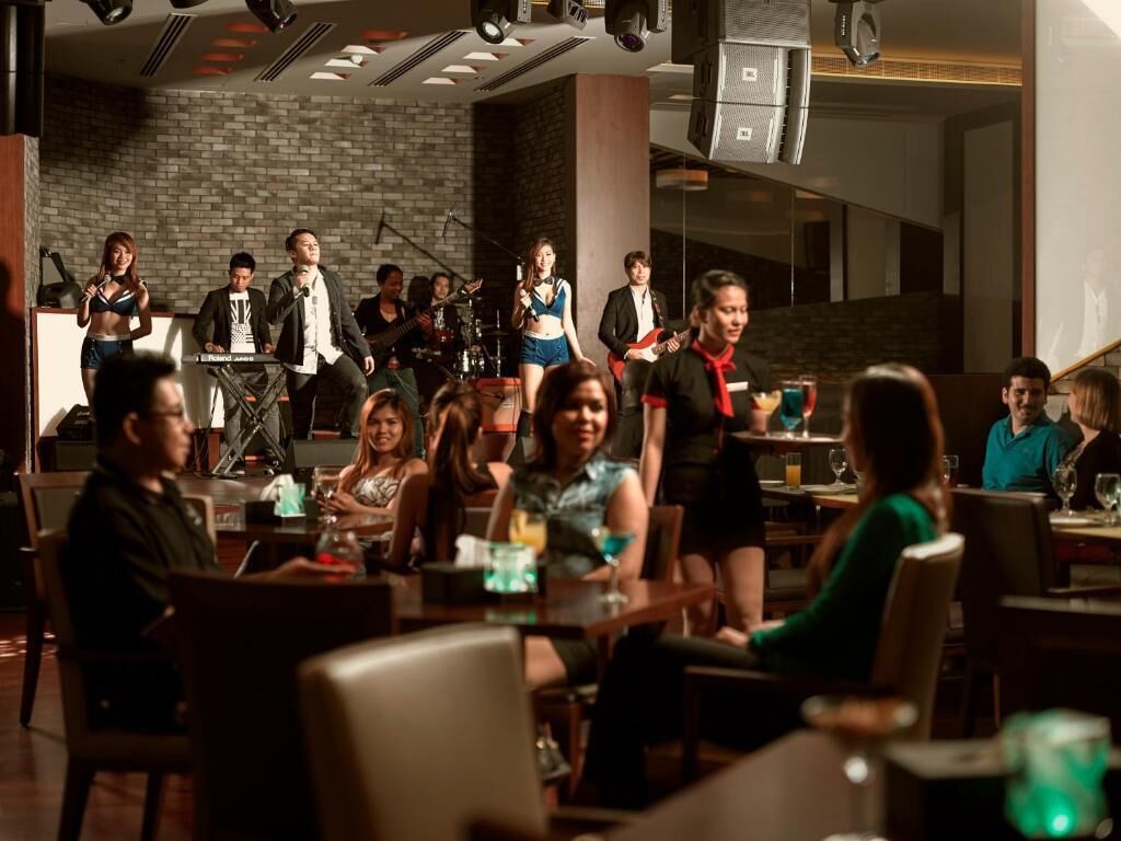 A restaurant with a stage for live music, tables with diners, and a brick wall in the background.