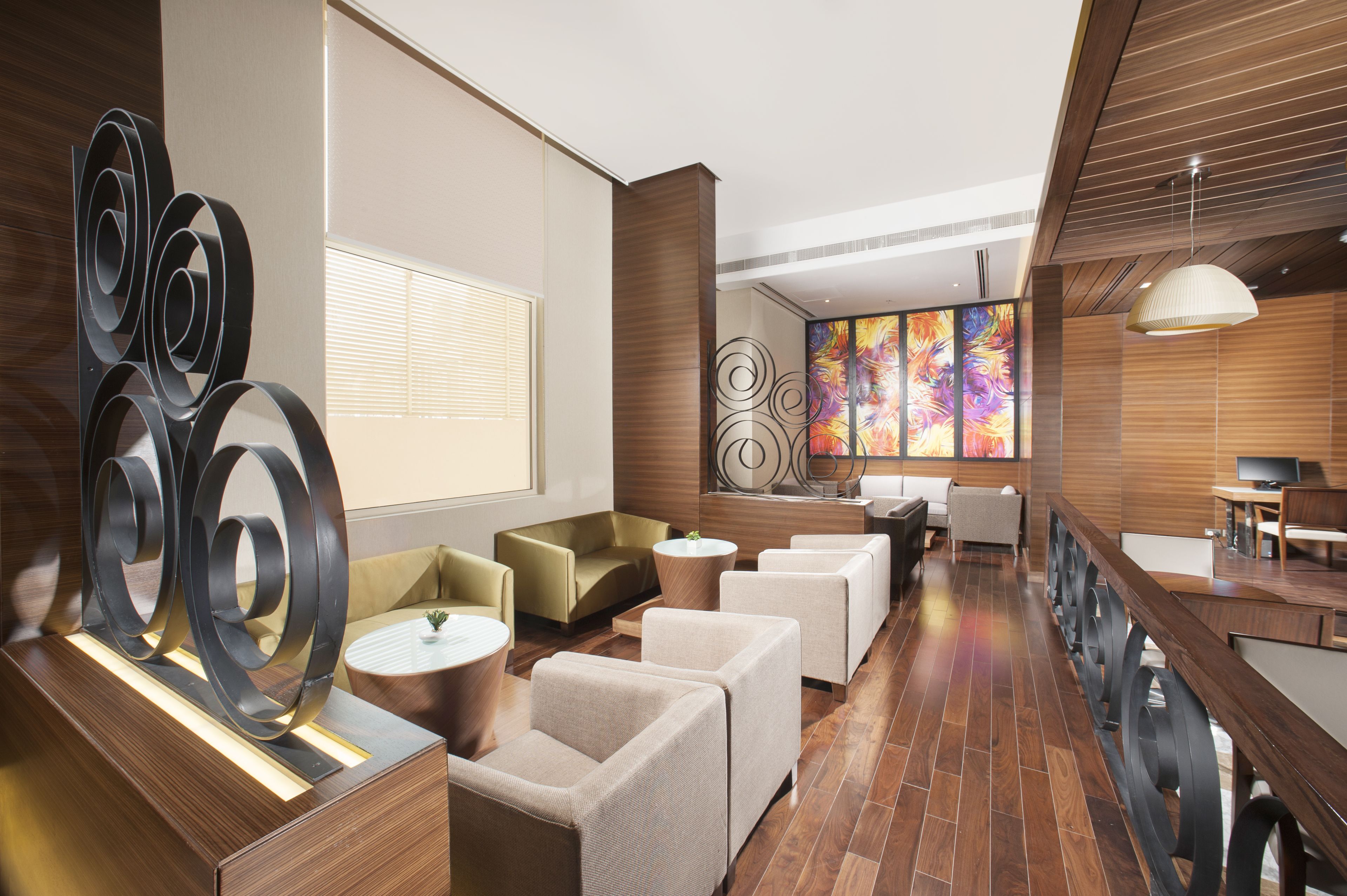 Un hall d’hôtel moderne avec un plancher en bois, des canapés beiges, une table basse ronde et un grand tableau abstrait accroché au mur.