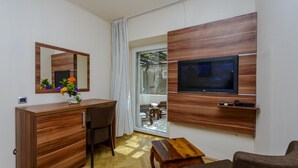 Una camera moderna con una scrivania in legno, una sedia, una TV a parete e vista all'esterno tramite una porta in vetro.