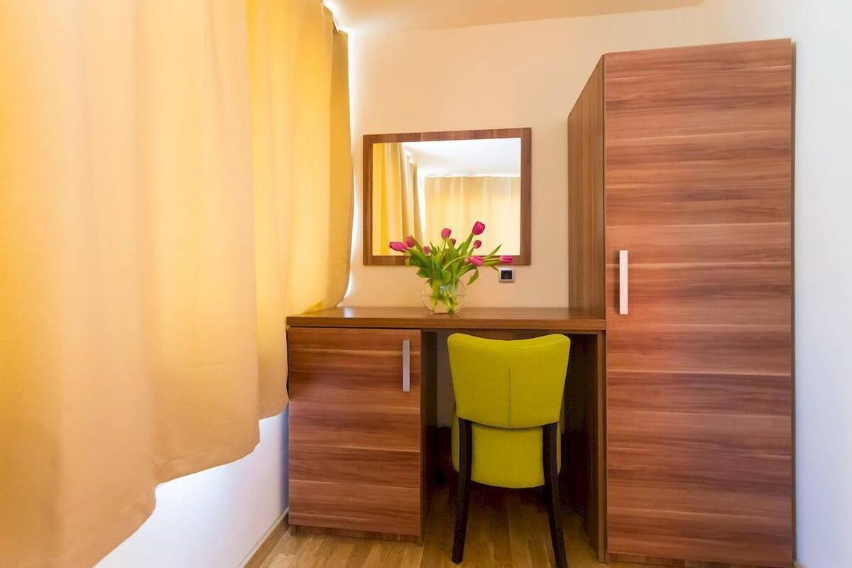 A compact room with a wooden desk, a chair, a mirror, and a vase with flowers.