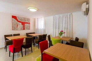 A hotel room with a dining area featuring wooden tables and chairs, a large abstract painting on the wall, and a window with curtains. - Villa Dorma (Dubrovnik)