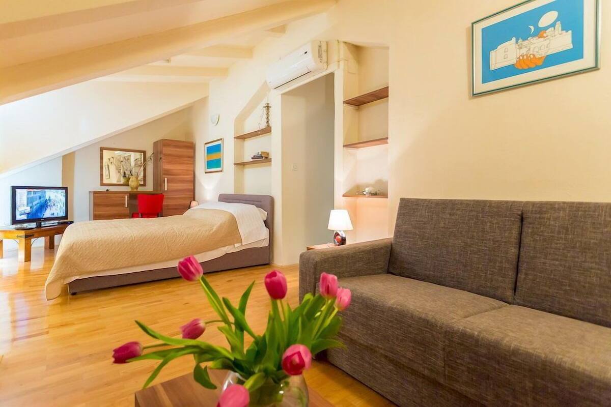 A modern bedroom with a bed, a sofa, a TV, and a vase of tulips.