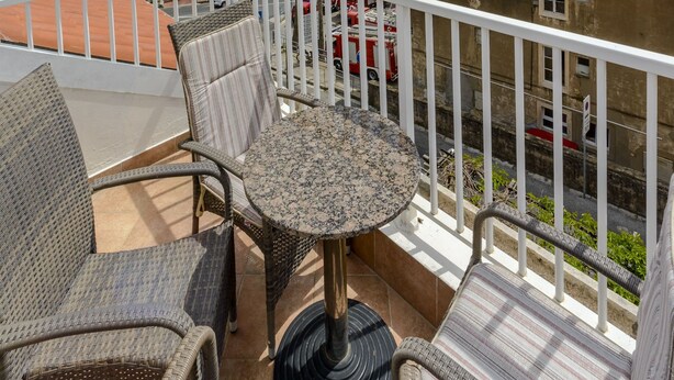 Un balcone con mobili in vimini e un tavolo, con vista su una località costiera con edifici e sullo sbocco del mare.