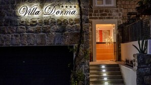Esterno di Villa Dorma, con facciata in pietra, insegna illuminata e scalinata che conduce all'ingresso.
