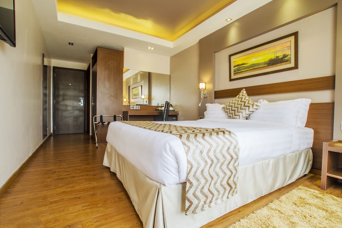 Une chambre d’hôtel avec un grand lit, un plancher en bois, un tableau au mur et un miroir au-dessus du lit.