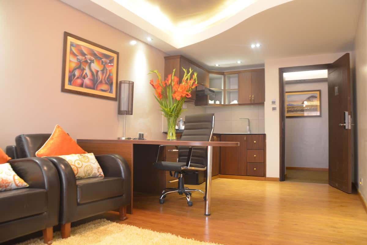 Un salon moderne avec un canapé, un bureau et une chaise. Il y a un tableau au mur et un vase rempli de fleurs sur le bureau.