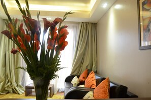 Una sala de estar con un sofá de cuero negro, cojines naranja y un jarrón con flores rojas.
