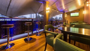 Una zona de bar con taburetes altos, una pantalla de televisión y vistas de la ciudad a través de amplios ventanales.