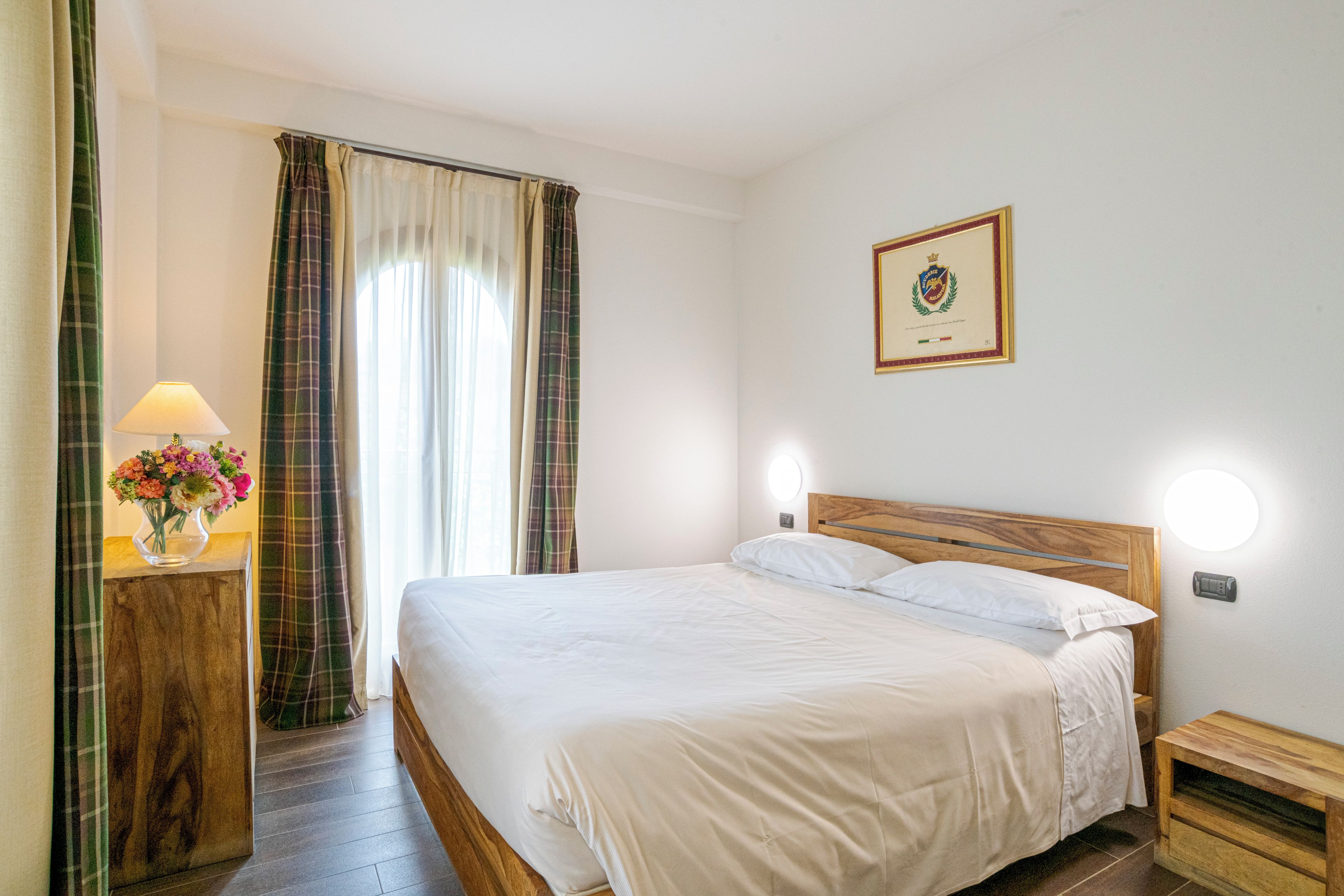A hotel room with a bed, a nightstand, a lamp, and a framed certificate on the wall.