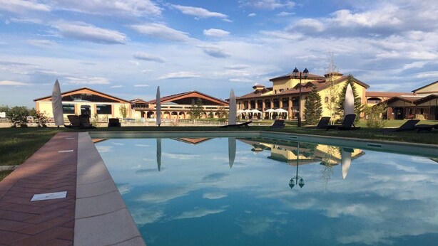 Una piscina con reflejo nítido, rodeada de edificios con tejados rojos y zonas de estar al aire libre.