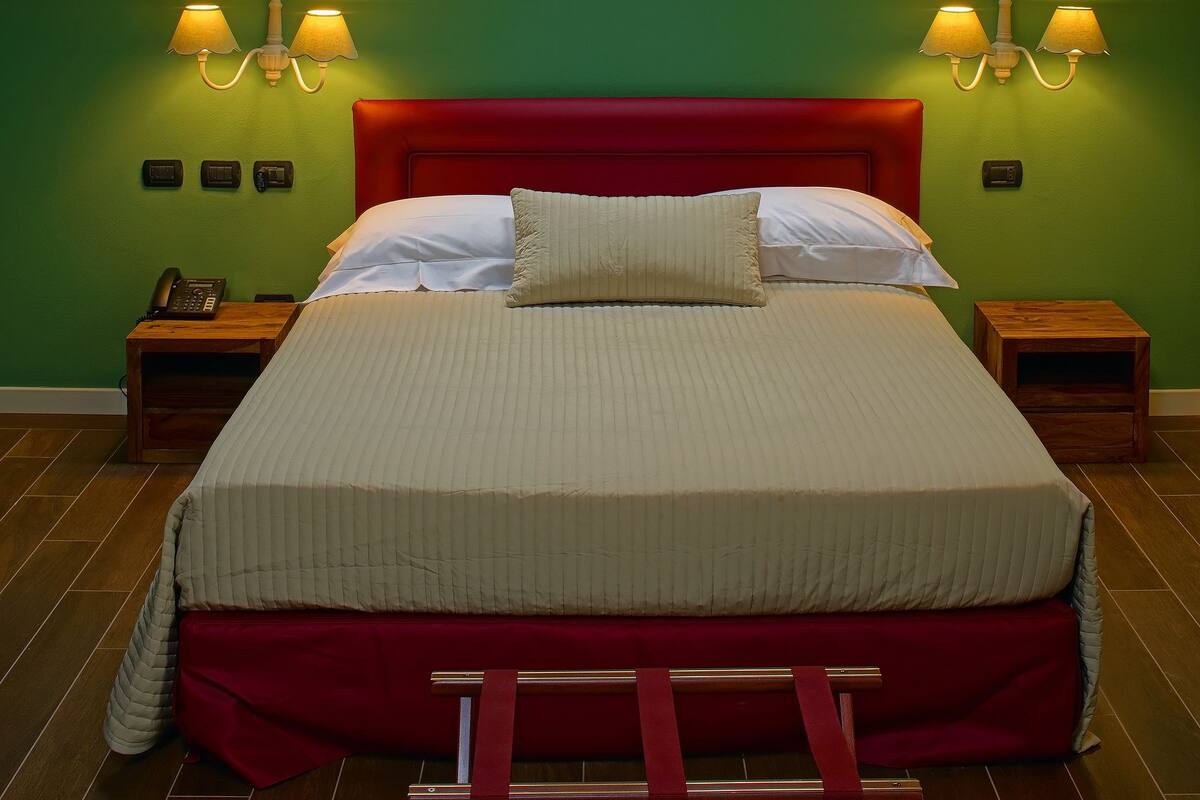 Quarto com cama grande, duas mesas de cabeceira, cabeceira vermelha e um claraboia acima.