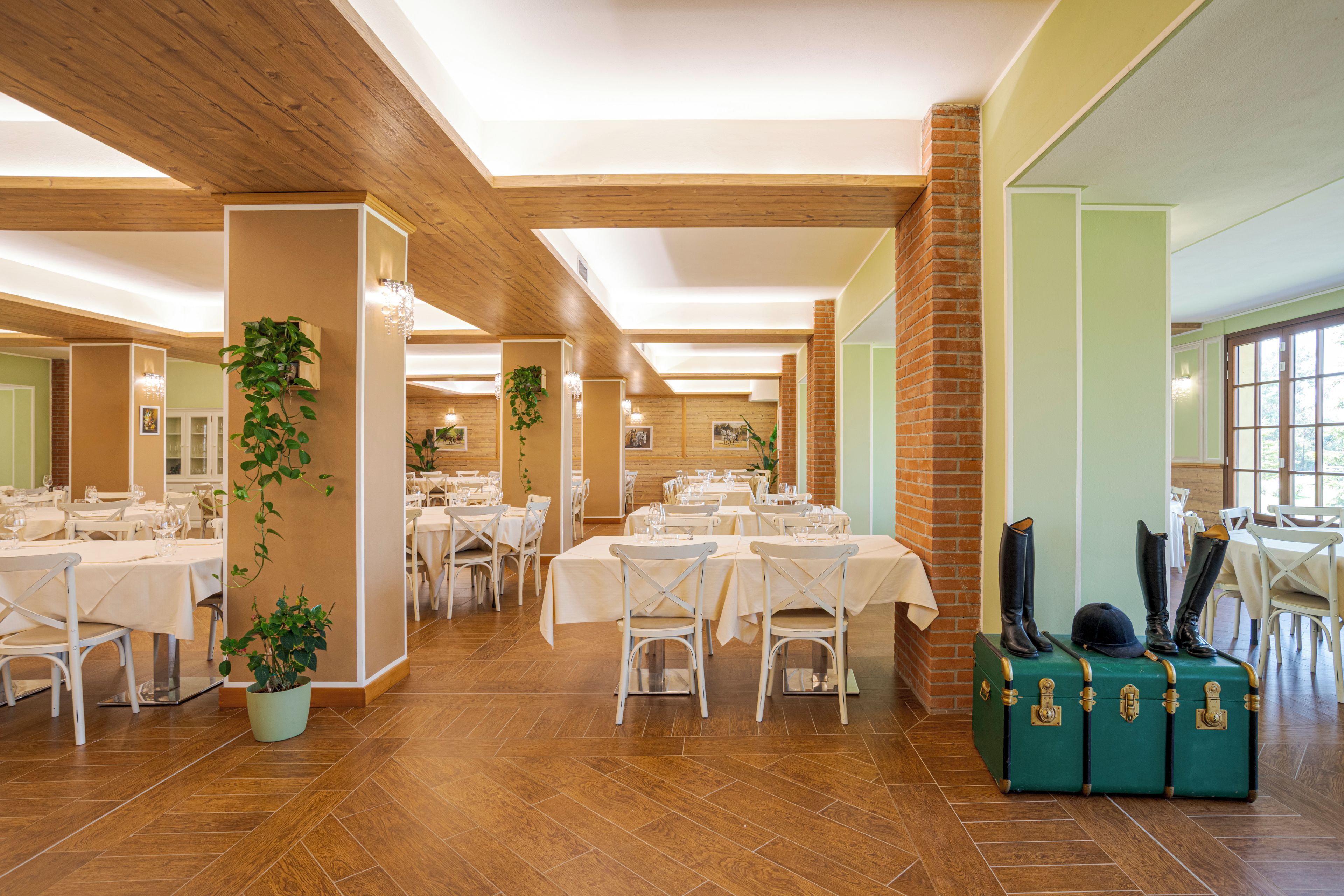 Un grand espace dédié à la salle à manger, avec plusieurs tables et chaises, des poutres en bois au plafond et des plantes en pot.