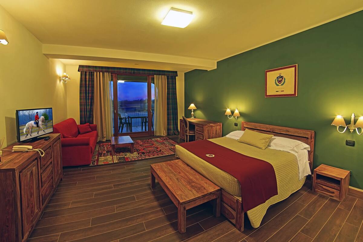 Quarto de hotel com cama, televisão, escrivaninha, cadeira e varanda com cortinas.