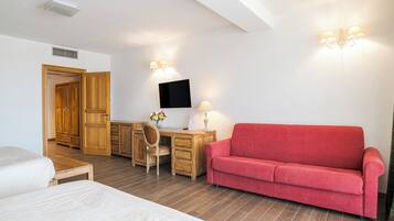 Una habitación de hotel con un escritorio de madera, un sofá rojo, una cama y un televisor montado en la pared.