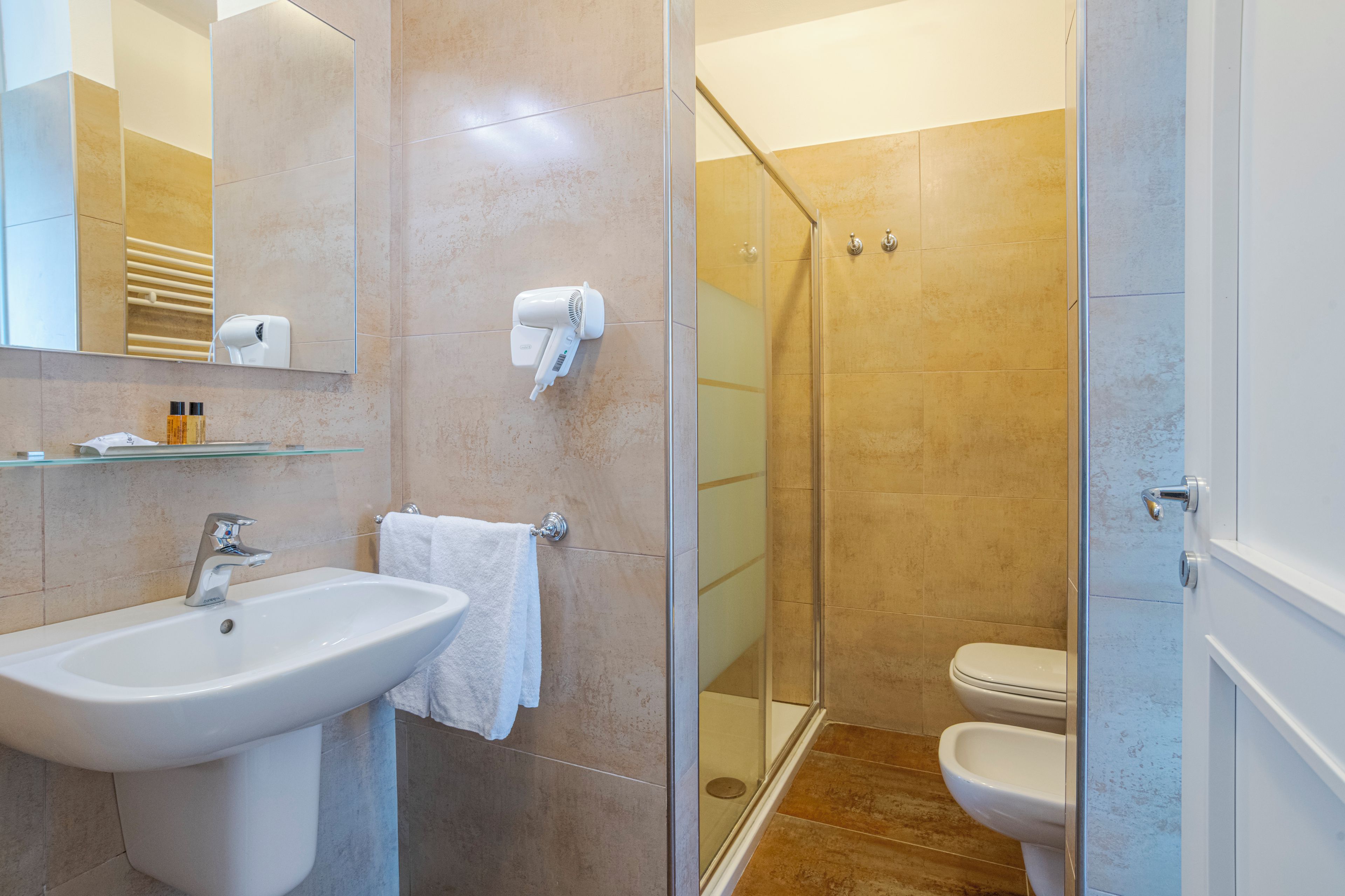 Un baño con lavamanos, espejo, toallero y zona de ducha con mampara de vidrio.
