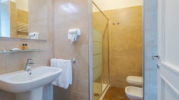 Un baño con lavamanos, espejo, toallero y zona de ducha con mampara de vidrio.