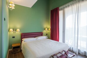 Habitación de hotel con cama, dos lámparas de noche, una mesita de noche, un banco de madera y una ventana con cortinas.
