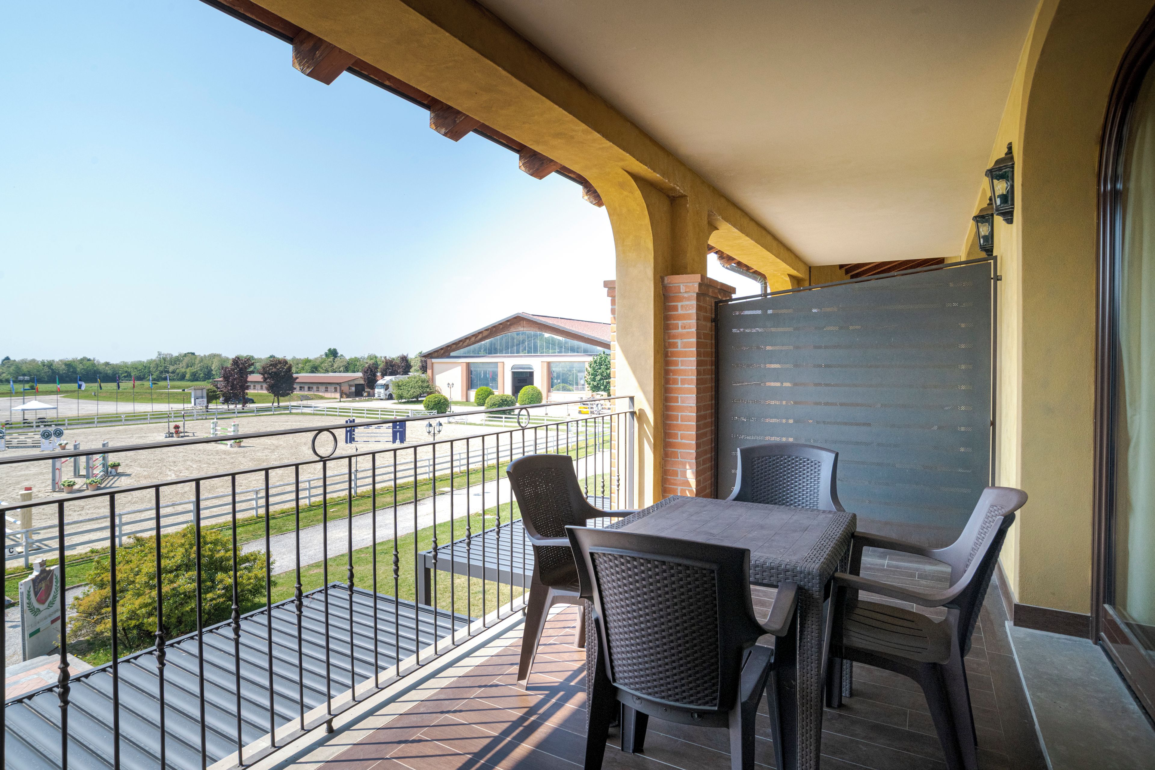 A balcony with two chairs and a table, overlooking a fenced area with a building in the background.