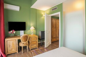 A hotel room with a bed, a desk with a chair, a TV, a wooden wardrobe, and a door leading to another room. - Agriturismo Il Boschetto (Ornago)