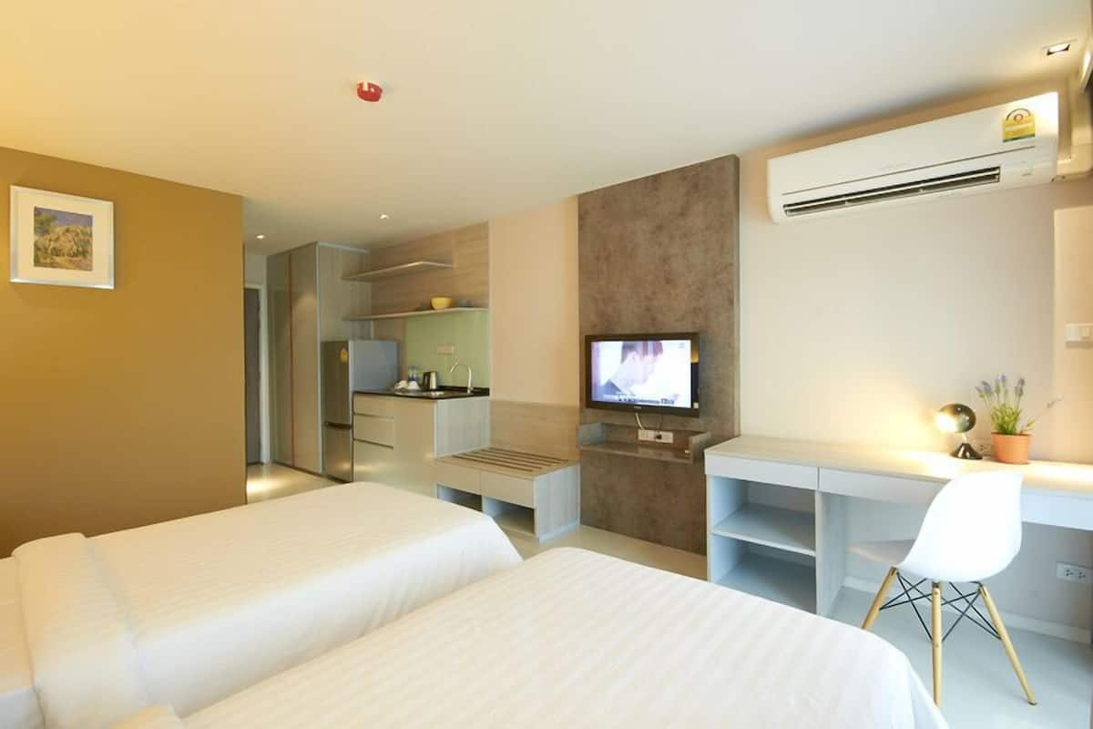 Ein Hotelzimmer mit zwei Betten, einem Schreibtisch, einem Fernseher und einer Klimaanlage.
