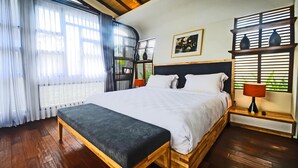 A bedroom with a large bed, wooden floor, and a window with blinds.
